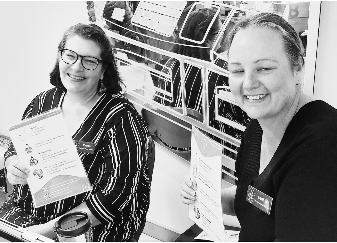 A photo of a founder Karen on the left and our General manager Ladina
Castle on the right, both smiling at the camera holding a paper copy of an example of Easy Read document, while at convention.