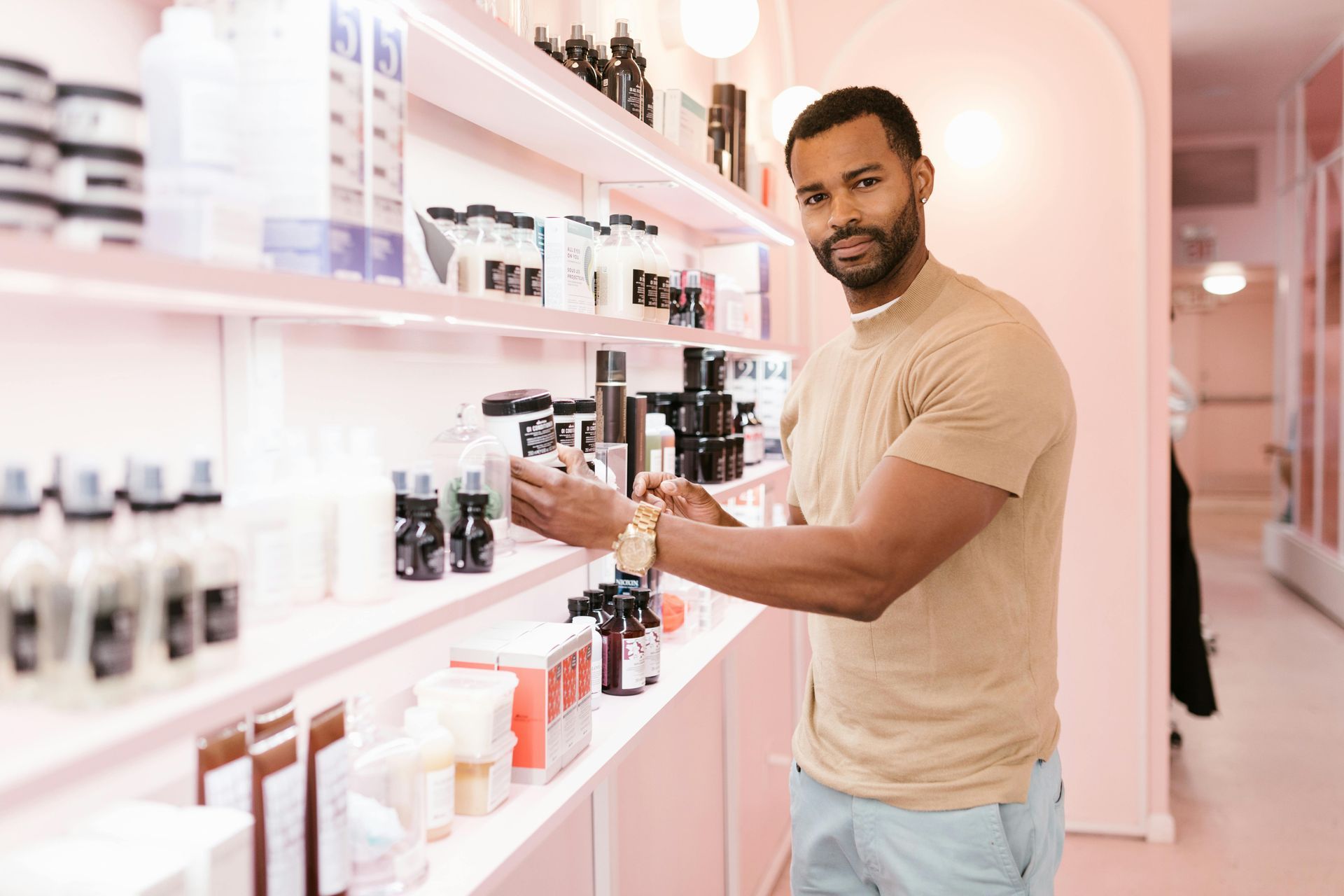 Man browsing hair products on a pink shelf in a salon.