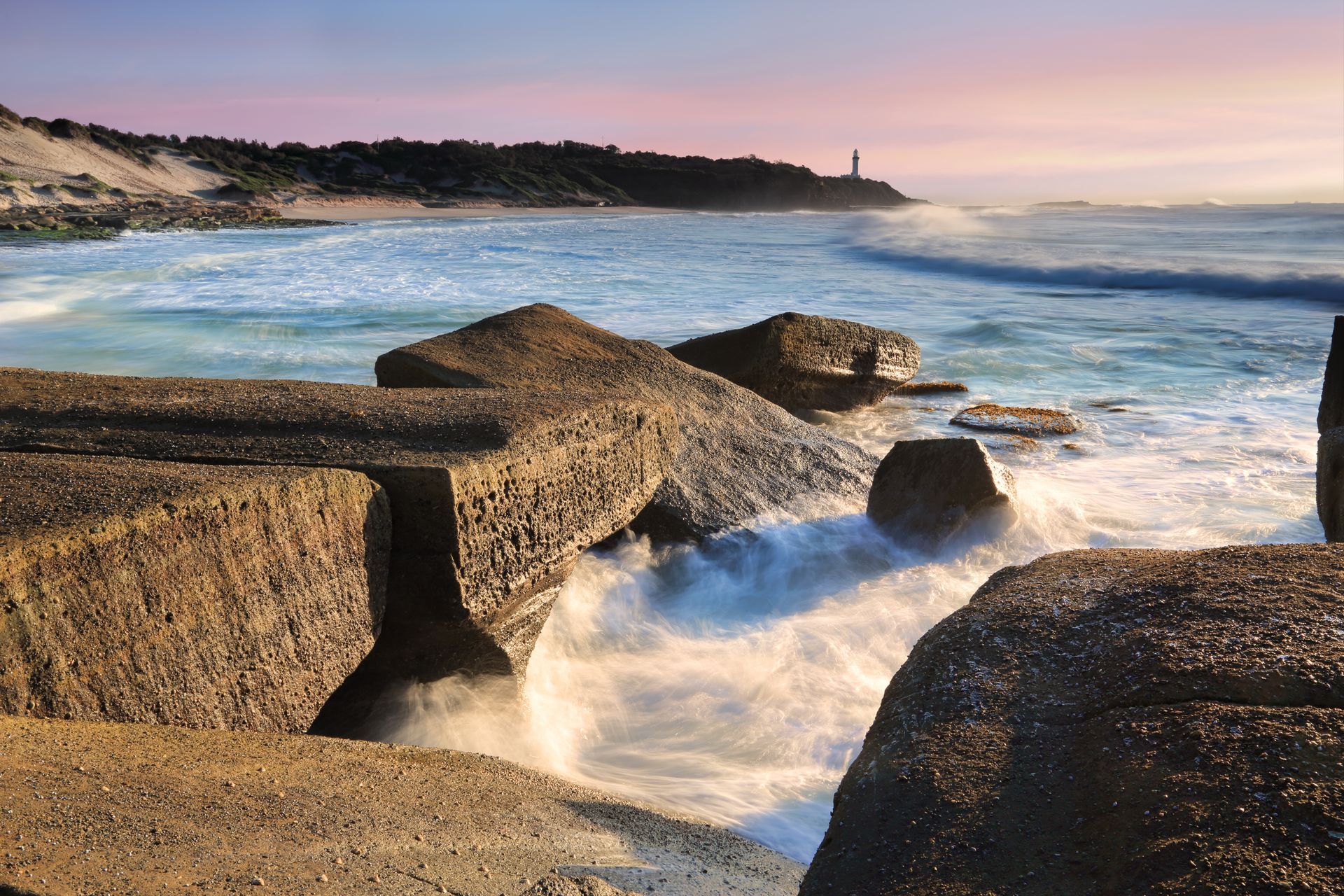 A Beach At Sunset, Featuring Waves Crashing Against Rocky Formations Under A Colourful Sky — Metric CNC In Central Coast, NSW