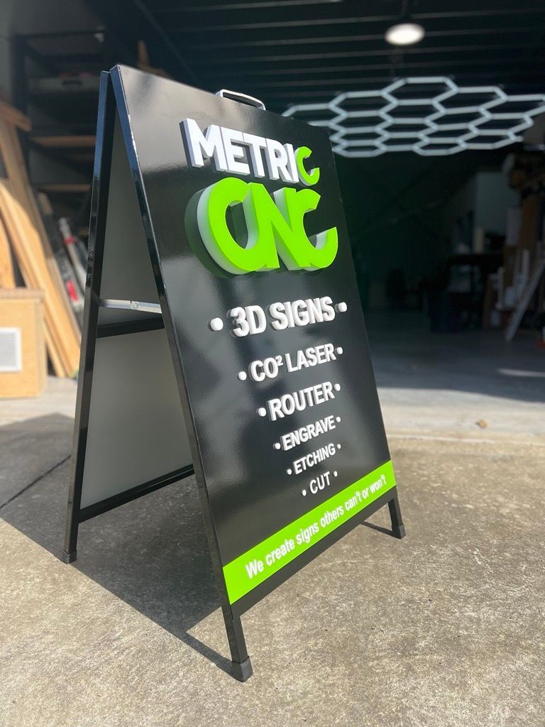 A Black and Green Sign is Sitting on a Sidewalk in Front of a Building — Metric CNC In Morisset, NSW
