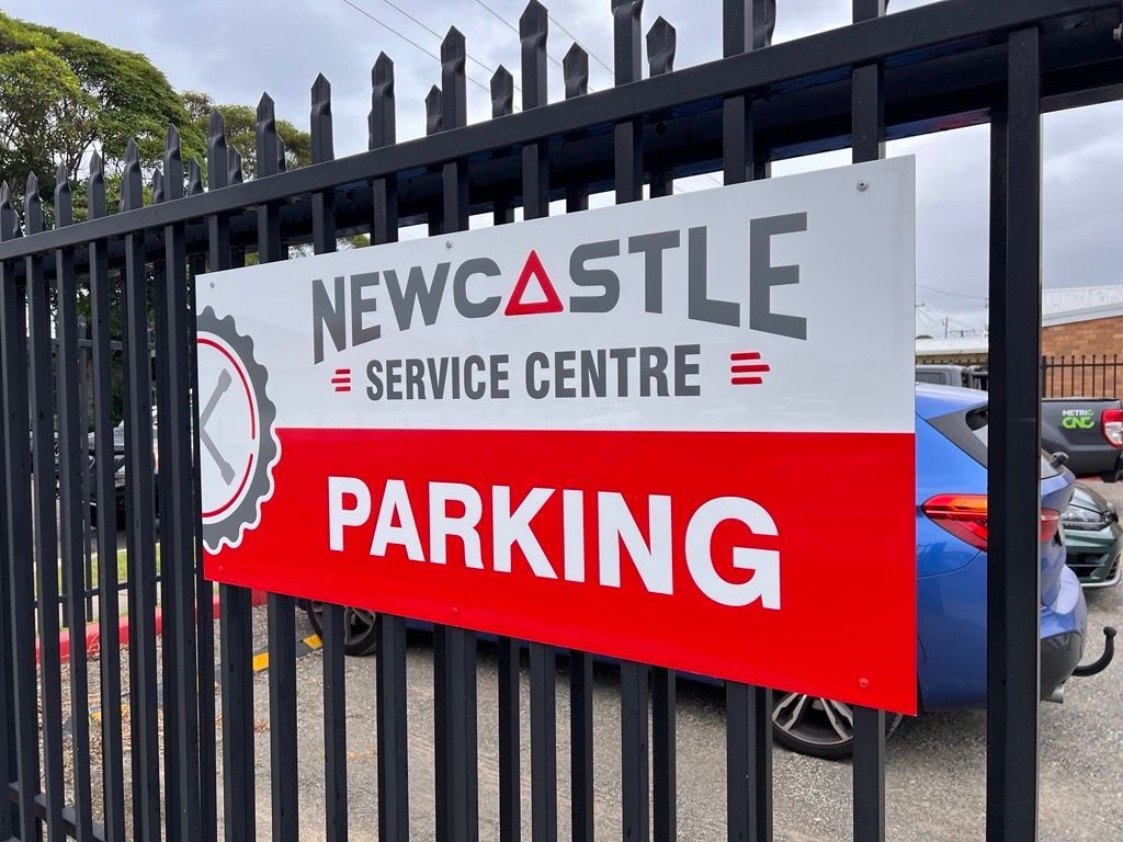 A Red and White Sign on a Fence Says Newcastle Service Centre Parking — Metric CNC In Morisset, NSW