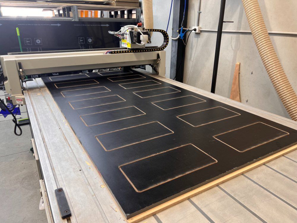 A Machine is Cutting a Piece of Black Plywood — Metric CNC In Morisset, NSW