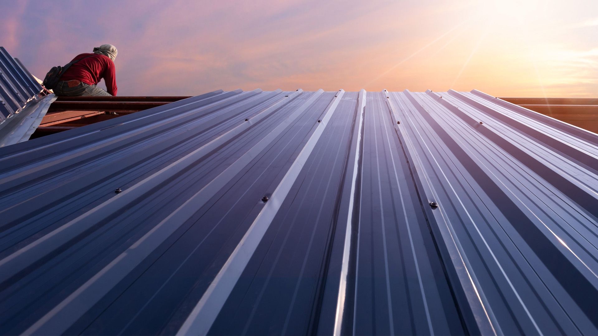 a man is sitting on top of a metal roof at sunset .