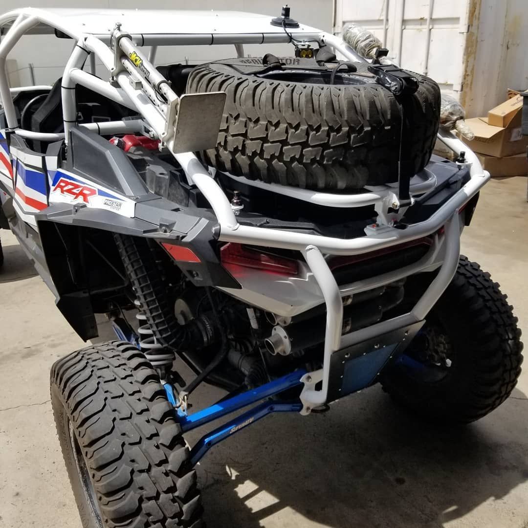 Off-road UTV with large tires and a spare tire on top, parked in a garage.