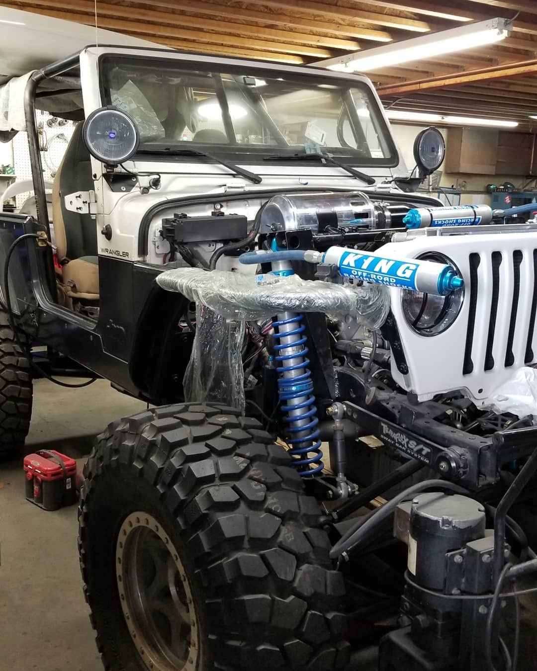 Lifted off-road Jeep in a garage, with large tires and exposed front suspension.