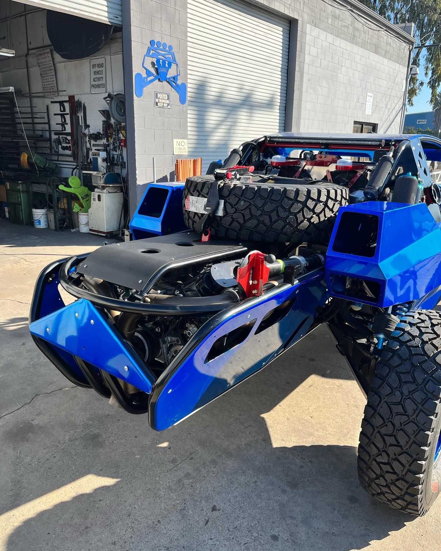 Blue off-road RC truck with oversized tires parked outside a garage, front view