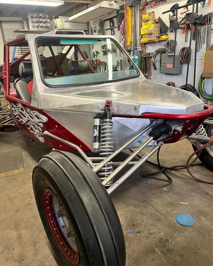 Custom red and silver dune buggy in a garage with exposed front suspension and large front tire