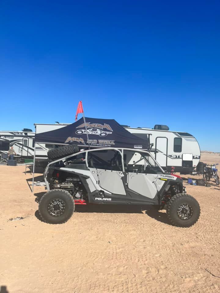 Off-road UTV with canopy parked in a desert campsite under a clear blue sky
