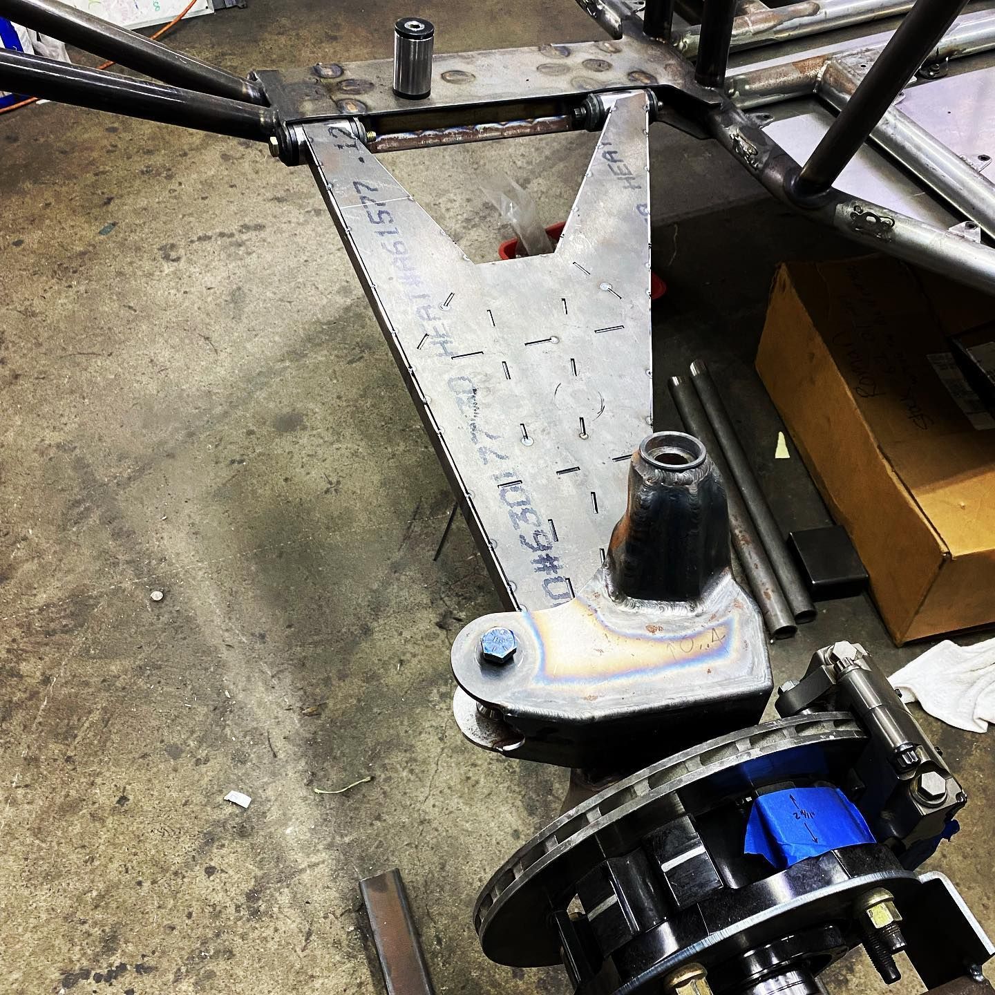 Metal chassis with V-shaped bracket and black wheel assembly on a workshop floor, with a blue component nearby