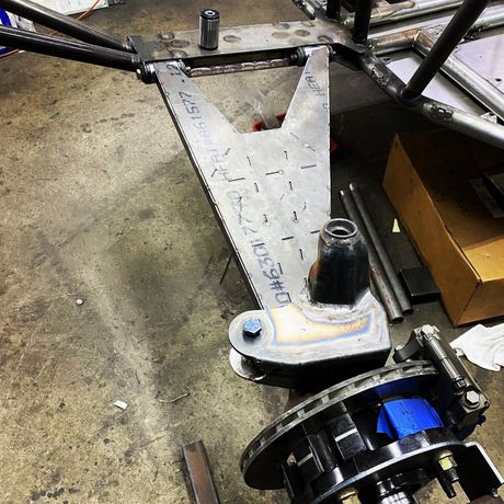 Damaged metal suspension arm on a workshop floor beside a black wheel hub and a cardboard box