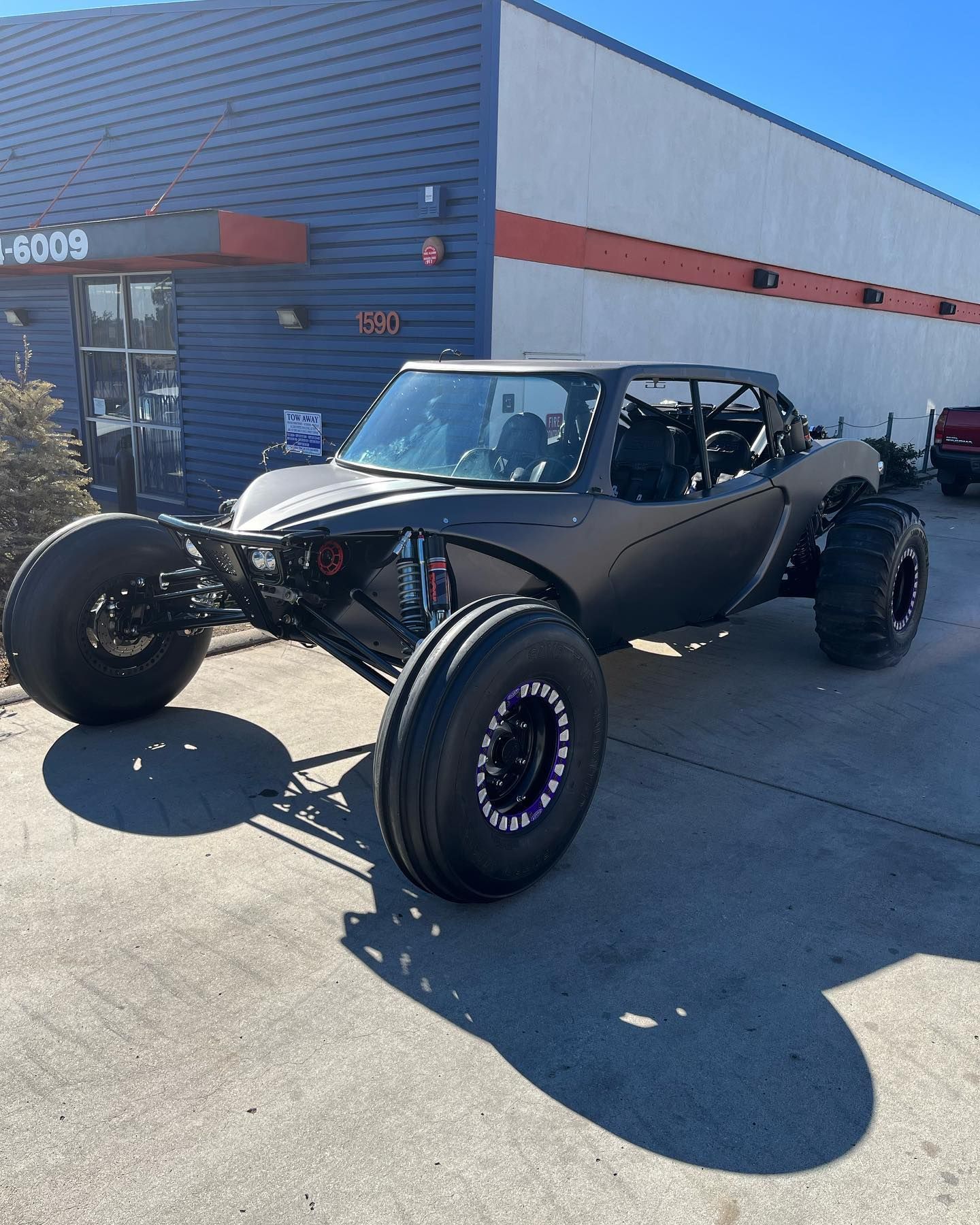 Black off-road dune buggy parked outside a building in daylight.