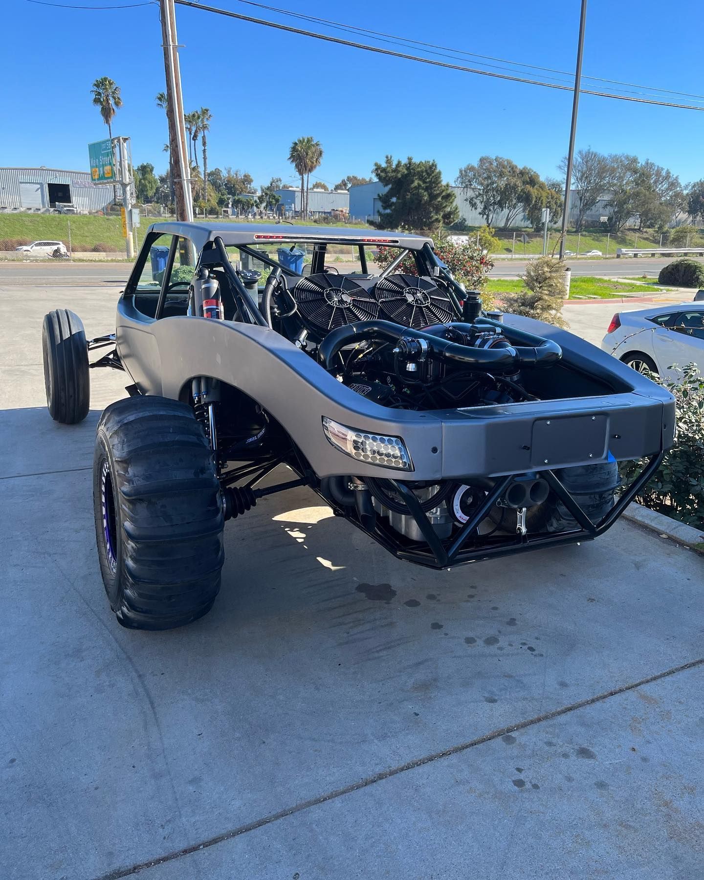 Off-road buggy with oversized tires and exposed engine parked under a carport