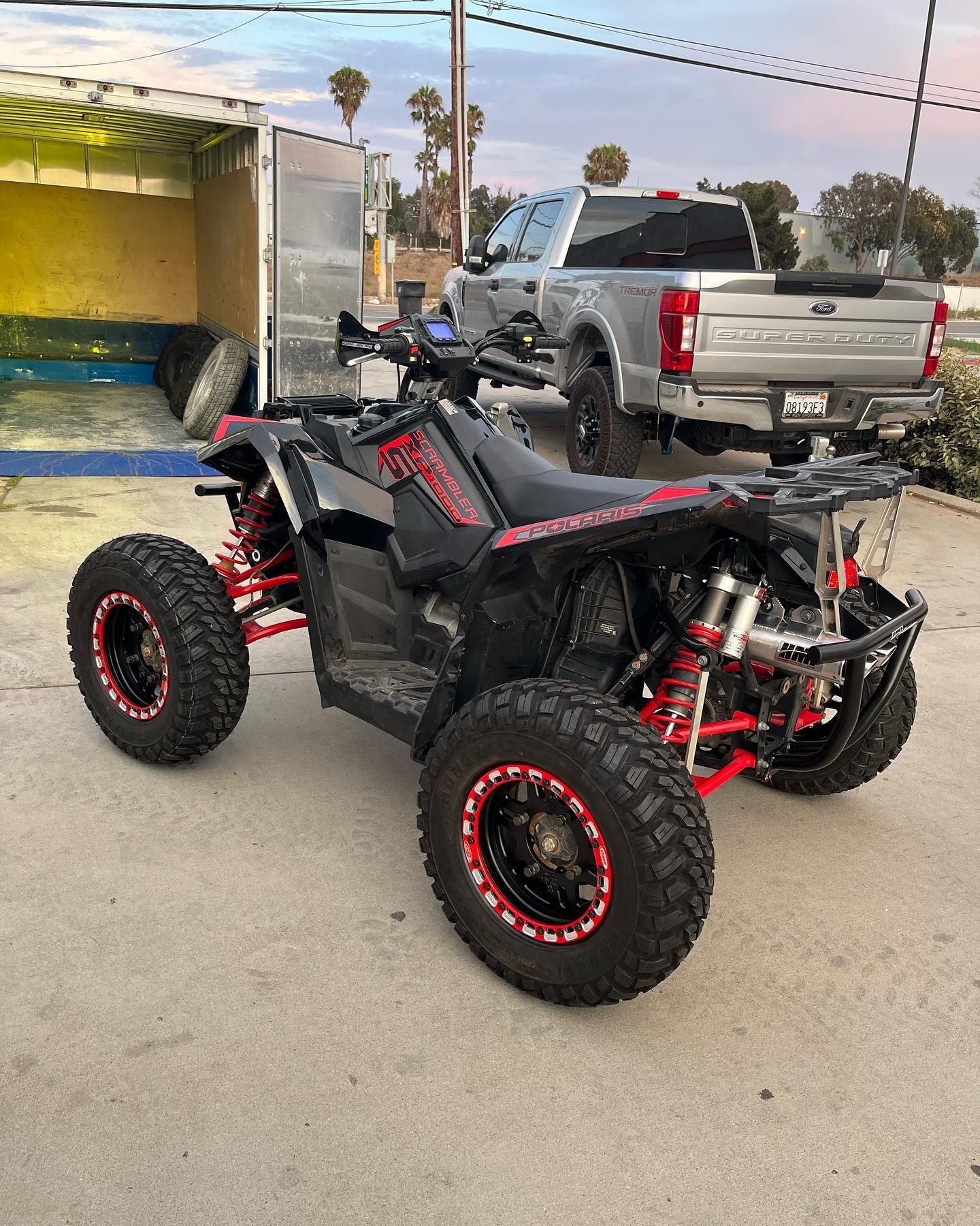 Black and red off-road ATV parked in a driveway beside a silver pickup truck.