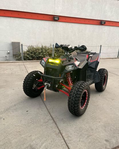 Black and red ATV with yellow headlights parked on a concrete driveway against a white wall