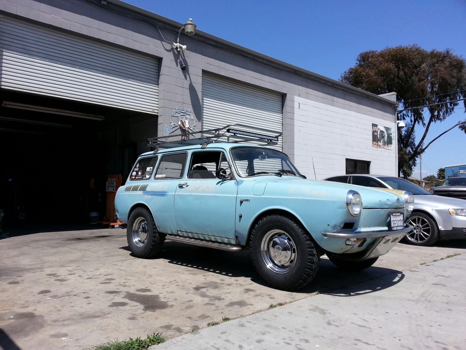 Light blue vintage SUV parked outside an auto repair shop under bright daylight