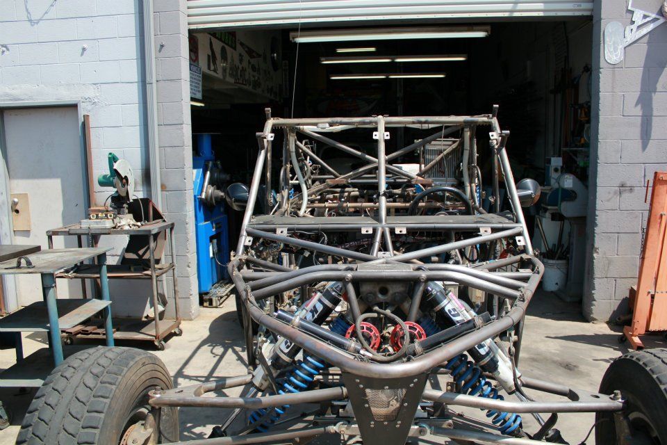 Race car chassis in a garage workshop, viewed from the front with exposed frame and wheels