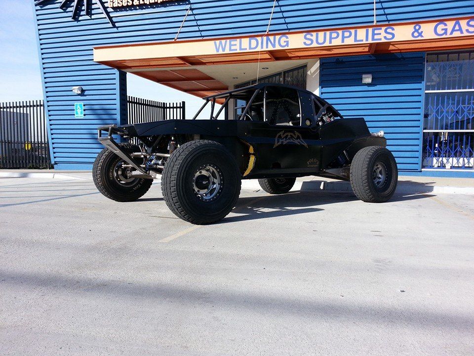 Black off-road dune buggy parked outside a welding supply shop under a blue awning