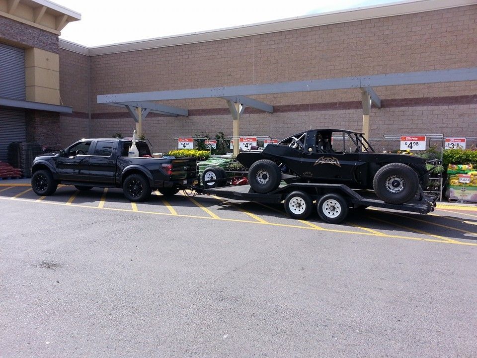 Two off-road vehicles on a trailer parked outside a brick building