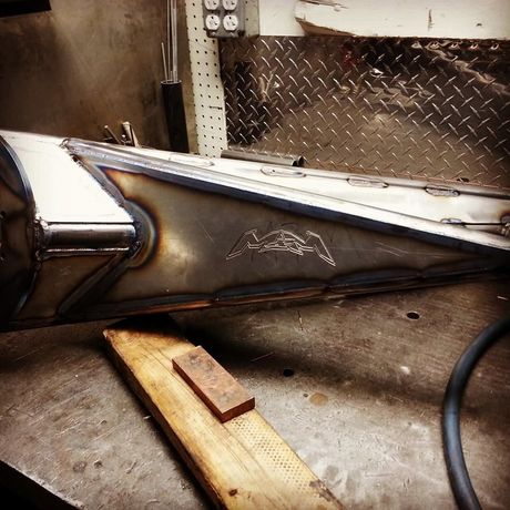 Welded metal car body panel with rust and a wooden support block in a workshop