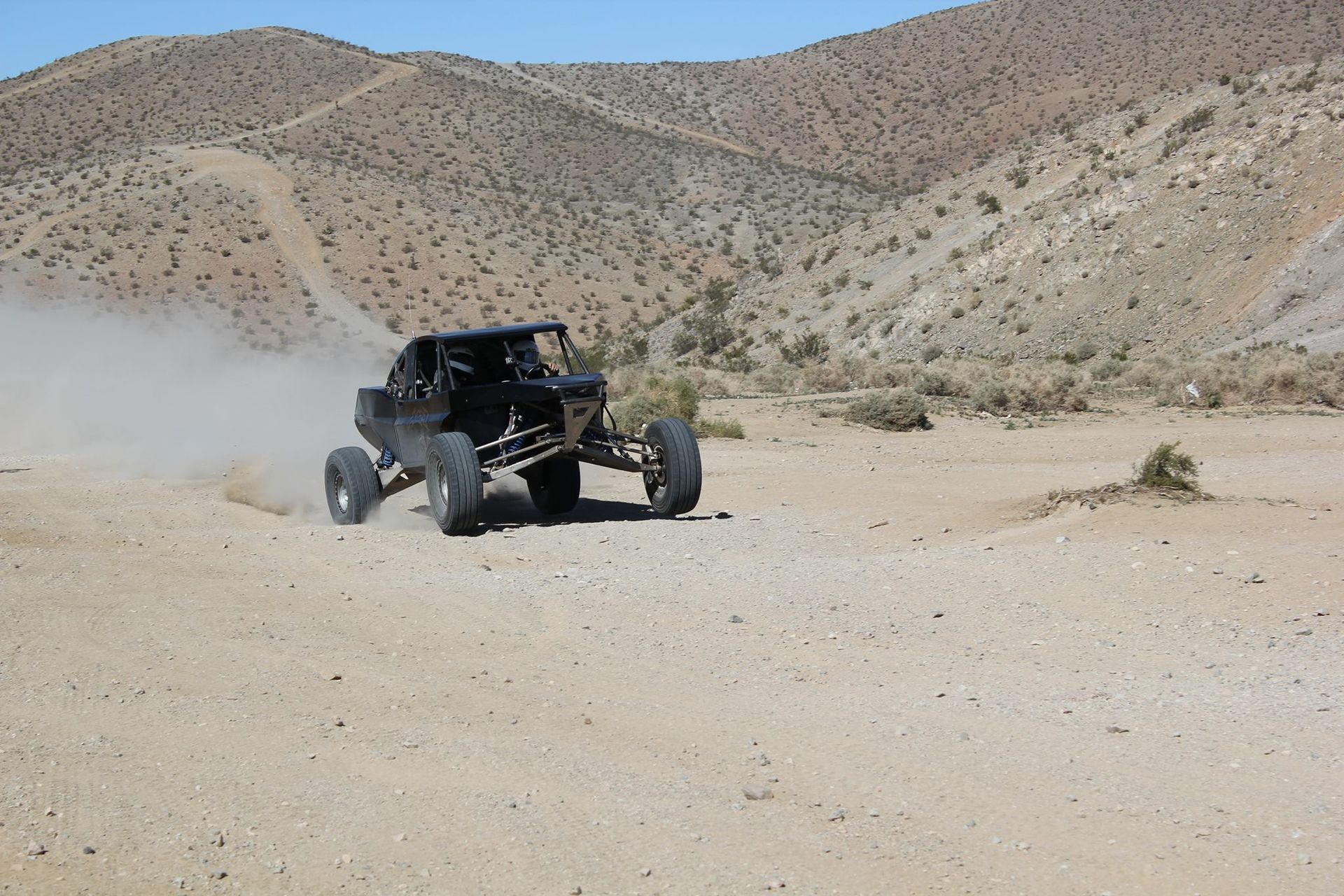Off-road buggy kicking up dust on a desert trail with rocky hills in the background