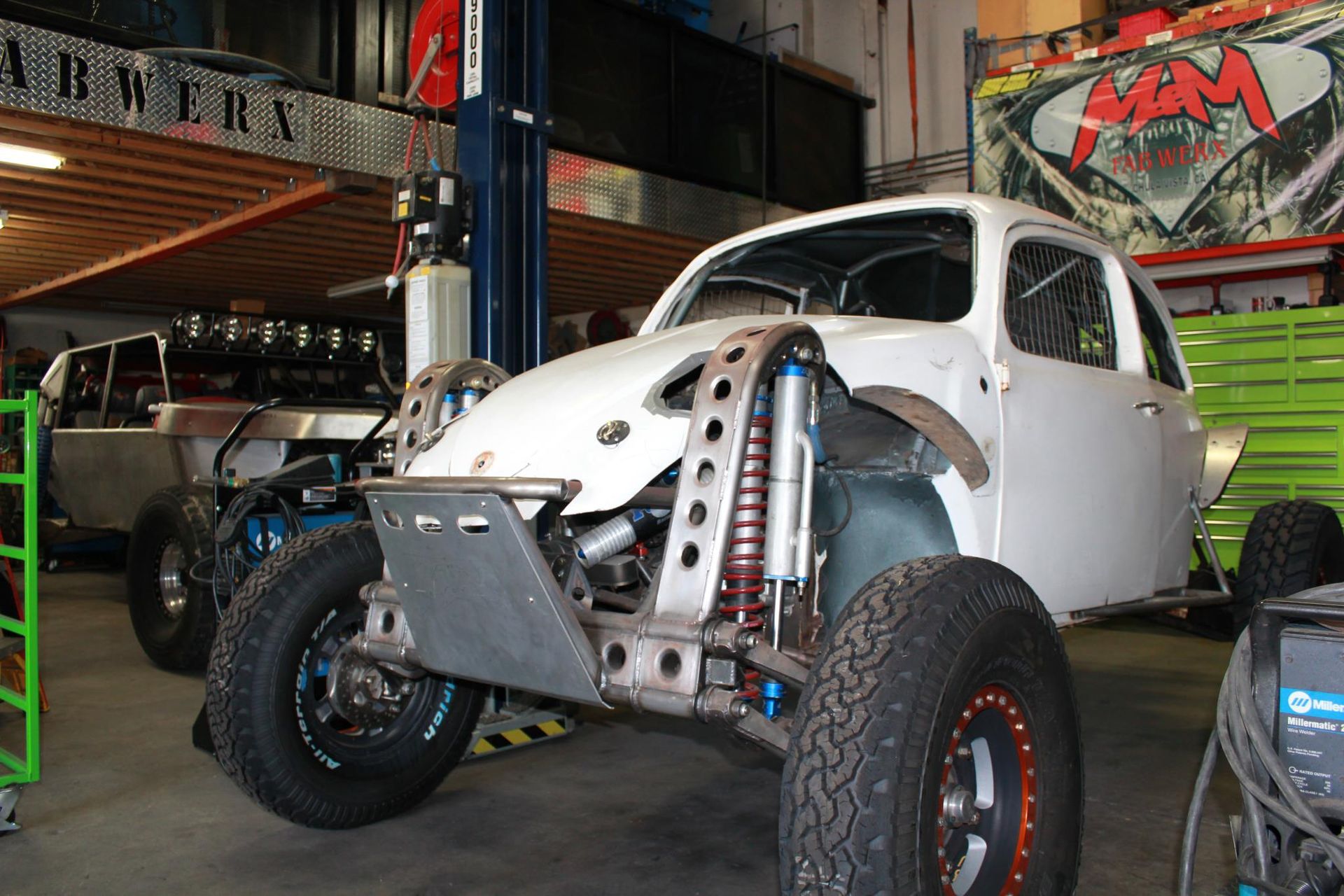 Modified white off-road buggy in a garage, front view with exposed suspension and large tires