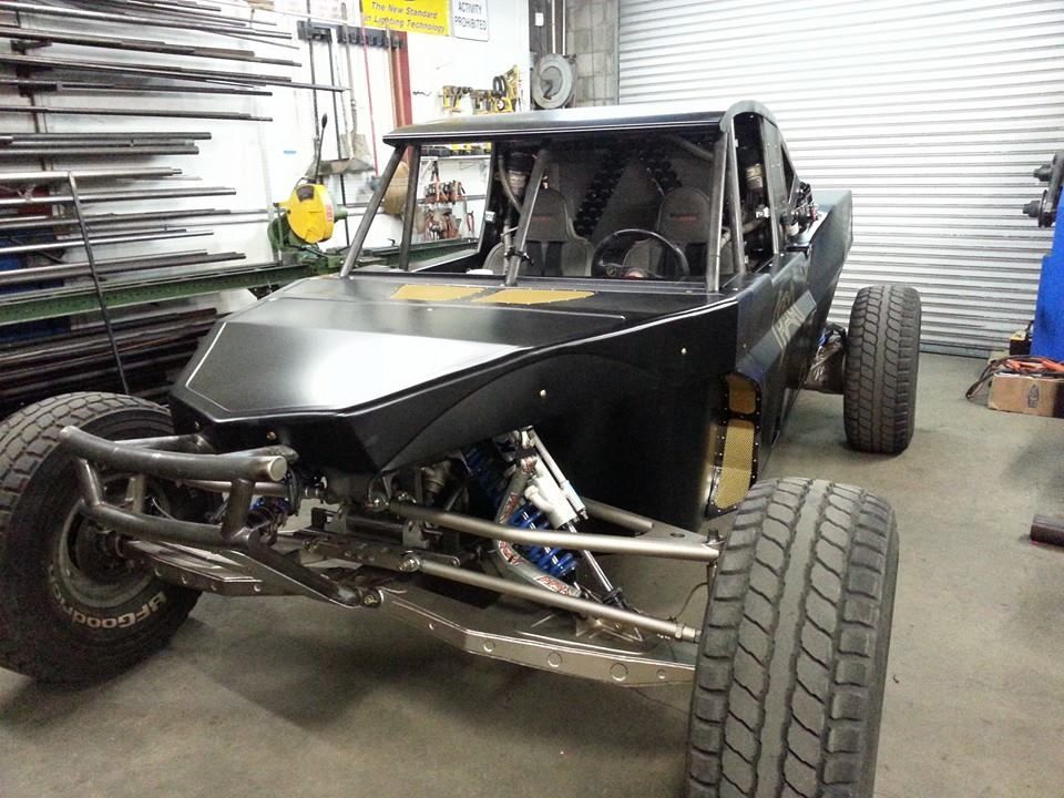 Black dune buggy with exposed frame and large off-road tires inside a garage workshop