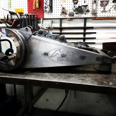 Large metal mechanical part on a workbench in a workshop, with tools hanging on the wall behind it.