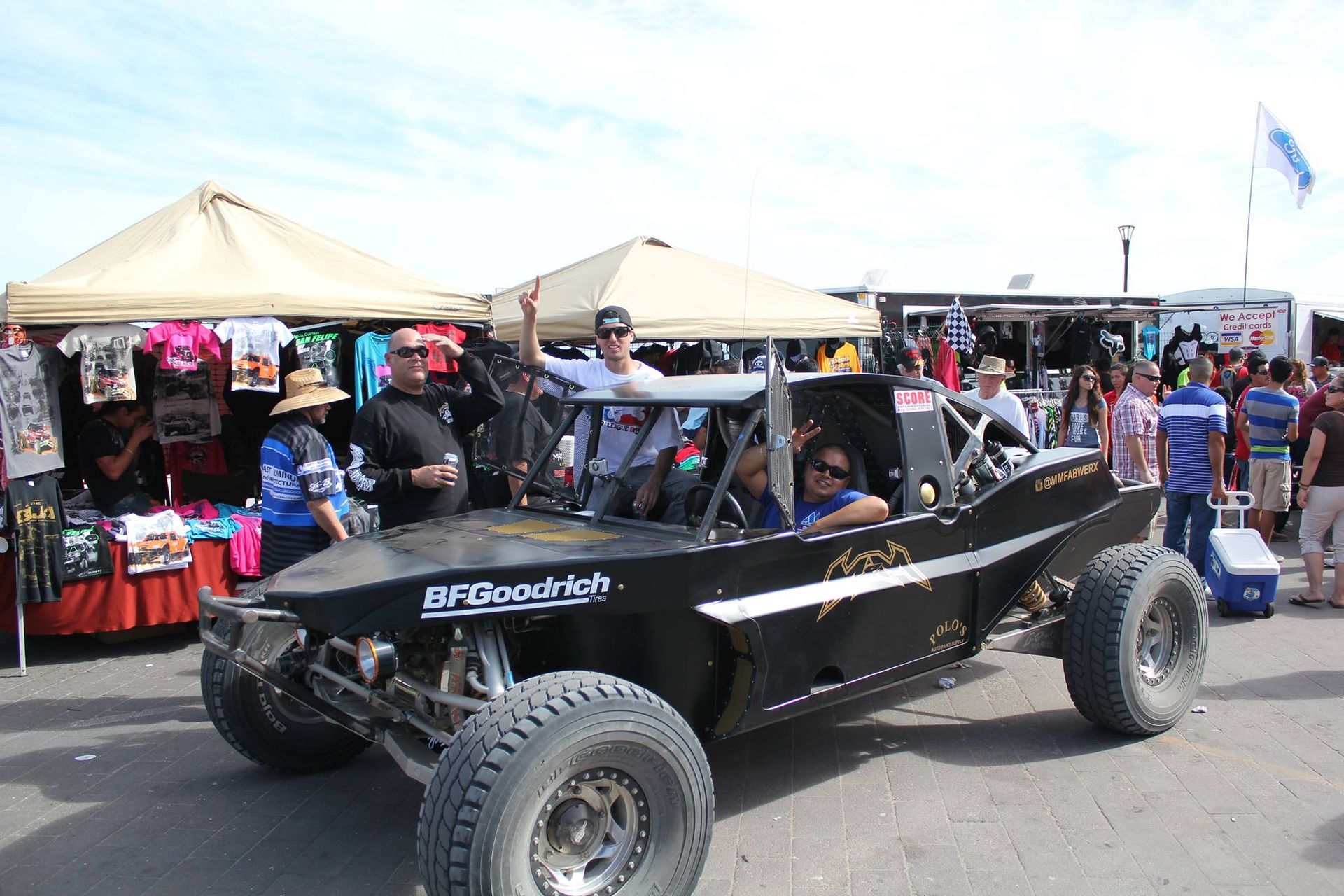 Black off-road buggy at an outdoor market with tents and crowds in the background