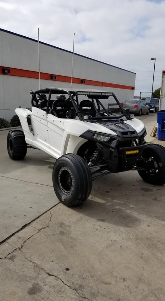 White off-road UTV with black roll cage parked on a concrete lot beside a gray building.