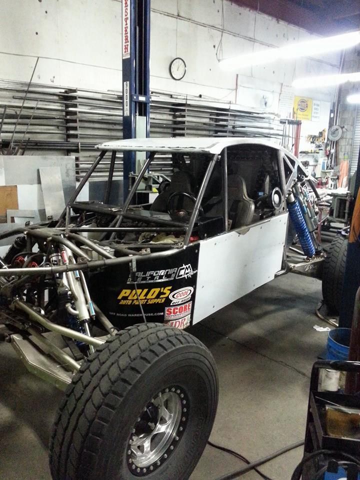 Off-road race buggy in a workshop, black and white with large front tire and exposed frame.