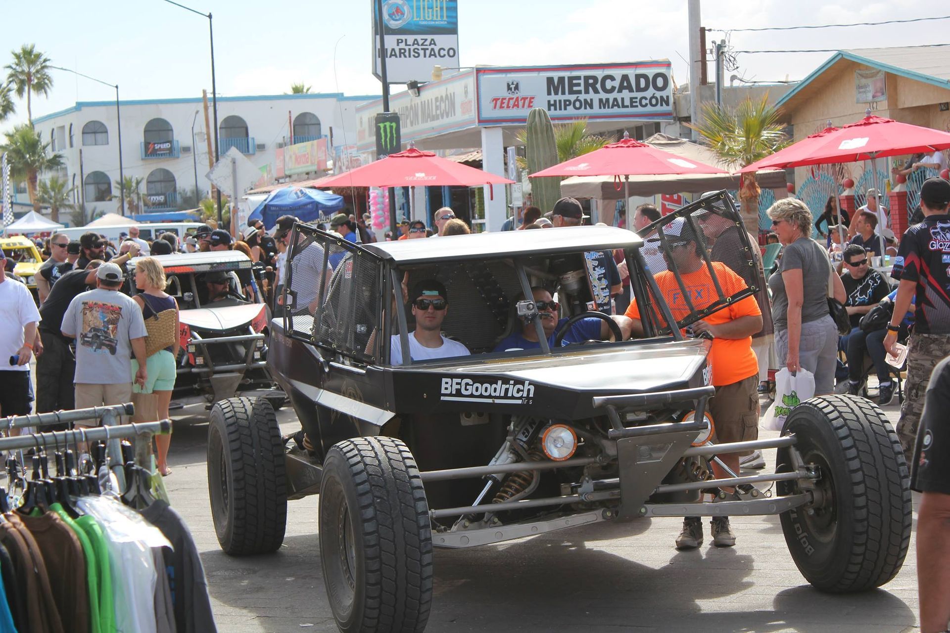 Off-road buggy at a crowded street event with spectators and red umbrellas