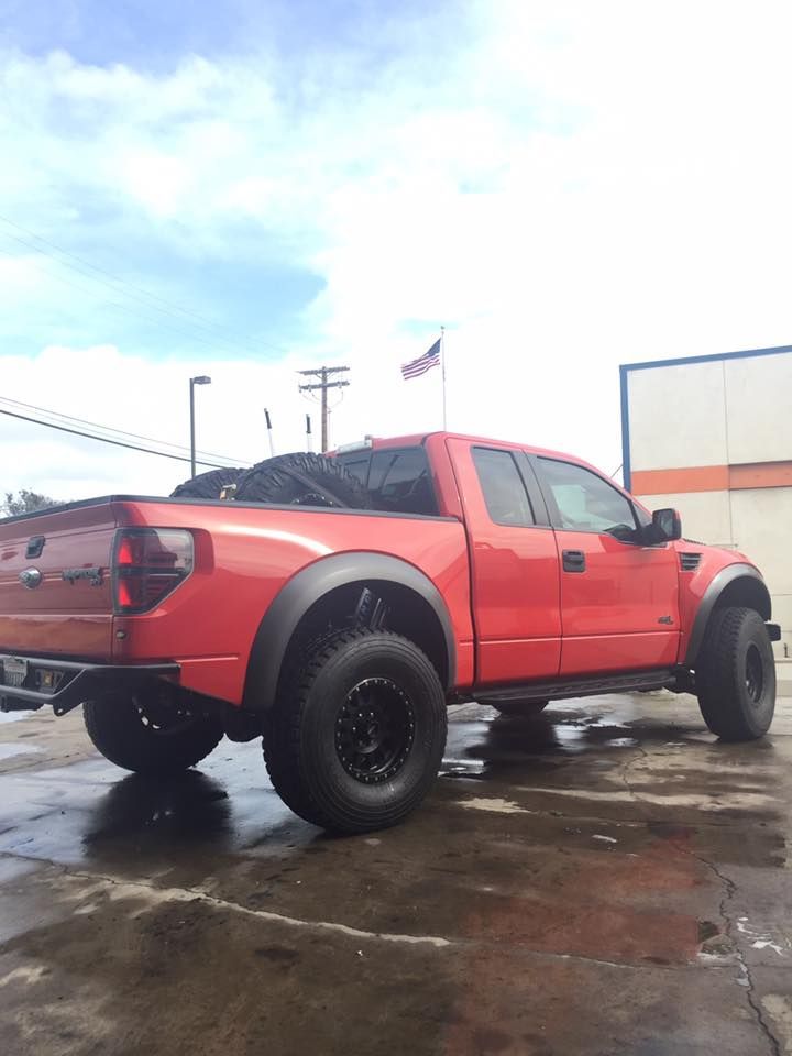Red lifted pickup truck parked on a wet lot under a cloudy sky