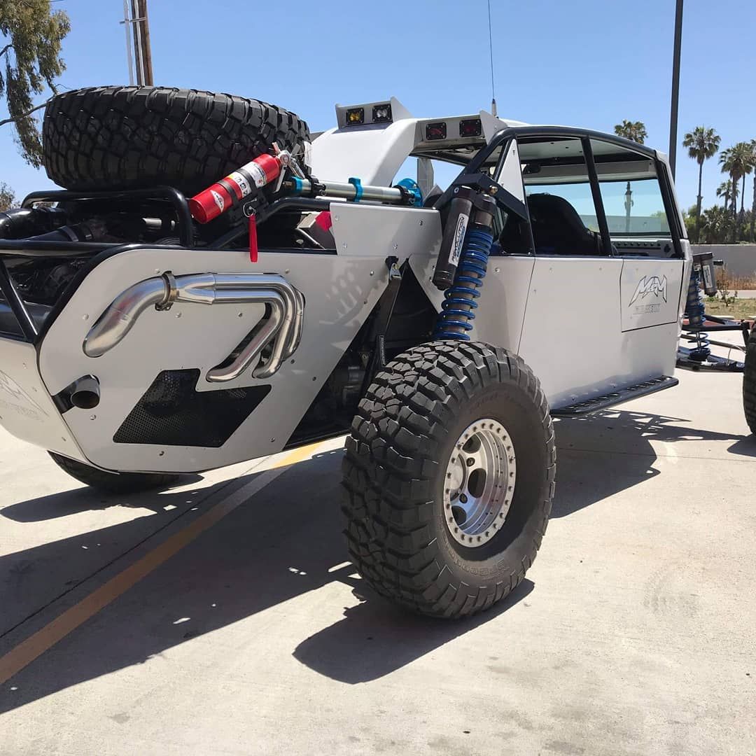 Modified off-road Jeep with oversized tires and spare tire parked outdoors in bright sun