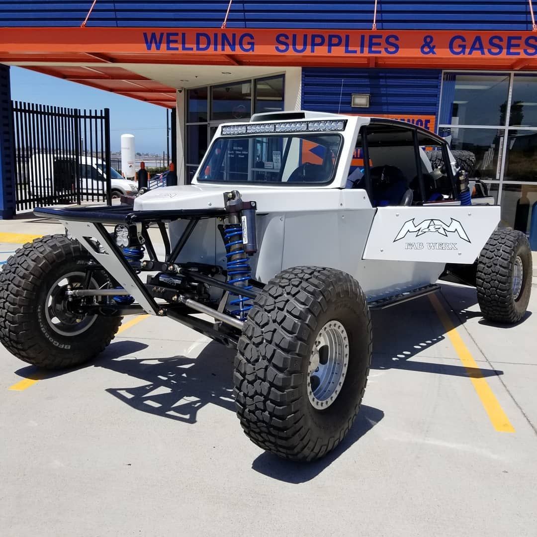 White off-road buggy parked outside a welding supplies store, with large tires and exposed suspension