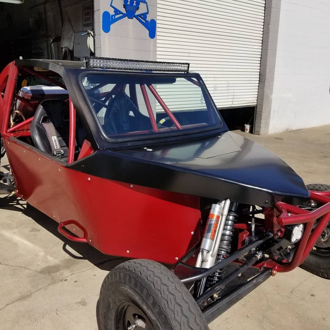 Red off-road buggy with black hood and roll cage parked outside a garage.