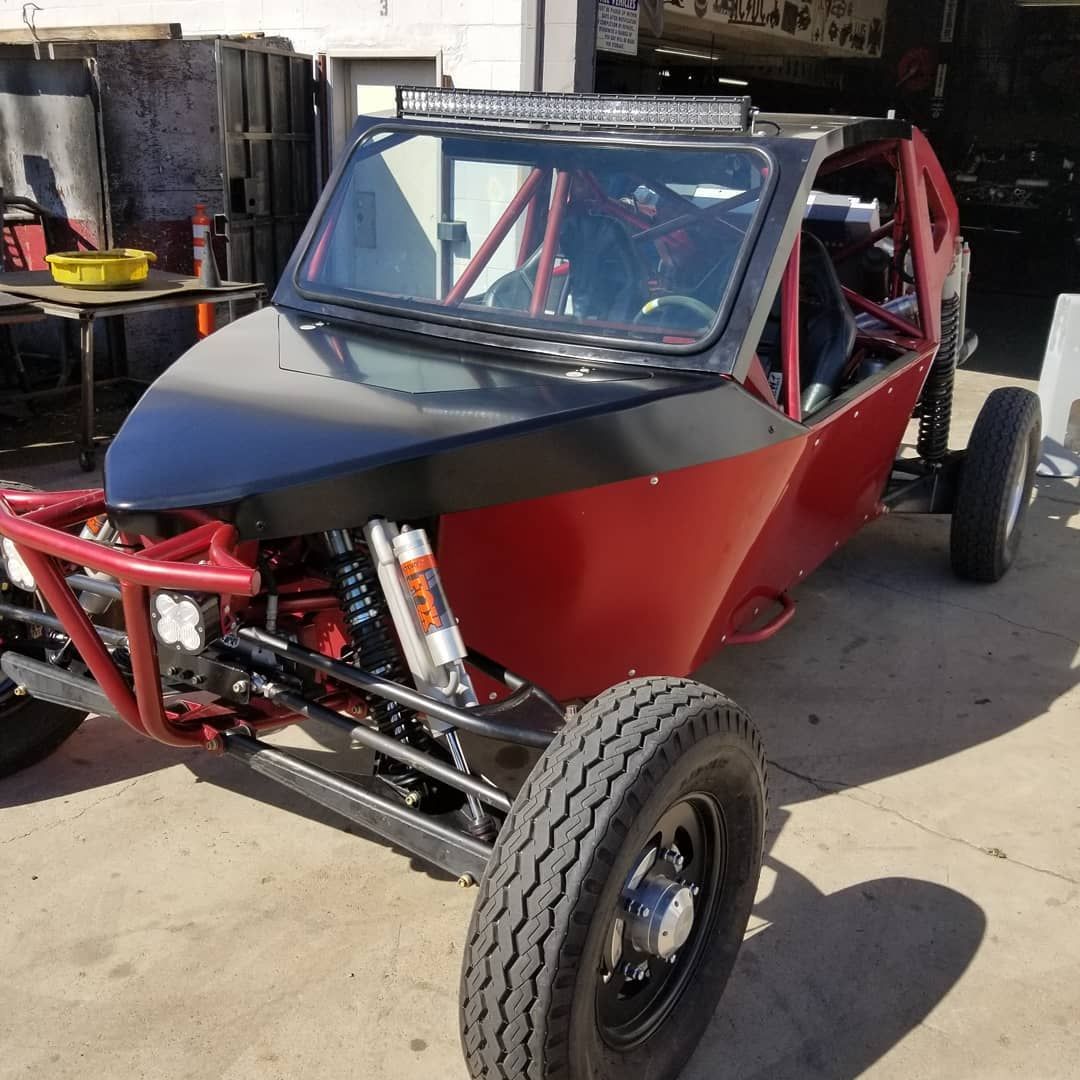 Red off-road buggy with black hood and roll cage parked in a workshop