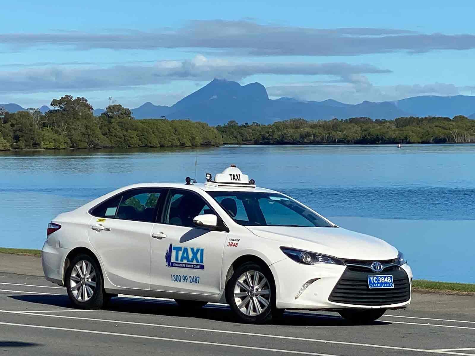 A White Taxi Is Parked In Front Of A Body Of Water — Kingscliff Tweed Coast Taxis Pty Ltd In Kingscliff, NSW