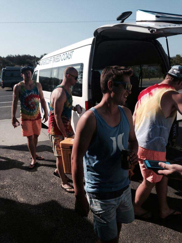 A Man Wearing A Hurley Tank Top Is Standing In Front Of A Van — Kingscliff Tweed Coast Taxis Pty Ltd In Kingscliff, NSW