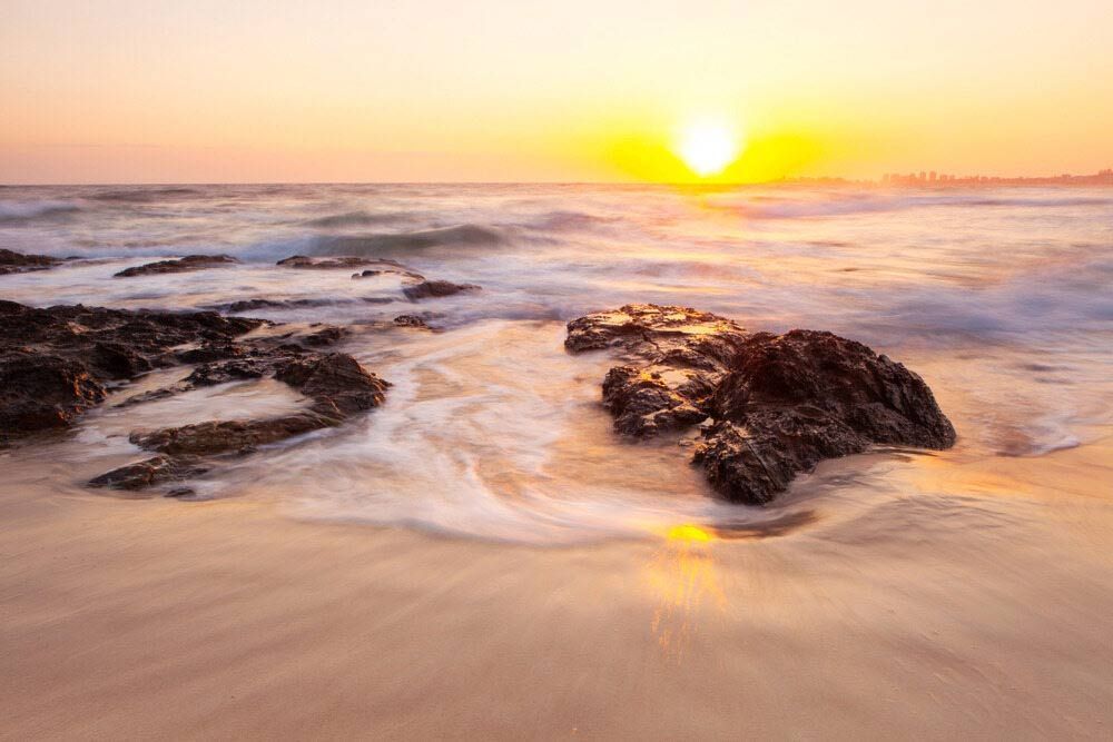 The Sun Is Setting Over The Ocean With Rocks In The Foreground — Kingscliff Tweed Coast Taxis Pty Ltd In Tugun, QLD