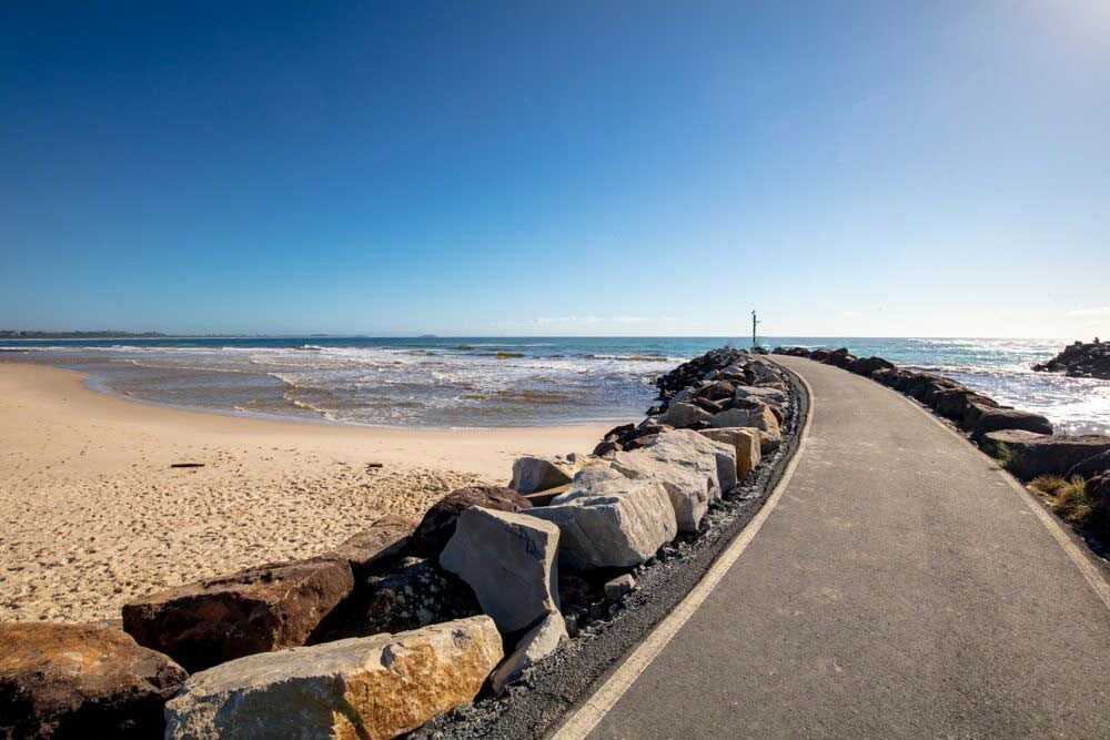 A Road Leading To The Ocean With Rocks On The Side Of It — Kingscliff Tweed Coast Taxis Pty Ltd In Chinderah, NSW
