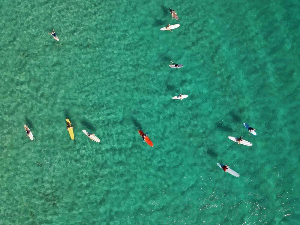 A Group Of People Are Riding Surfboards In The Ocean — Kingscliff Tweed Coast Taxis Pty Ltd In Coolangatta, NSW