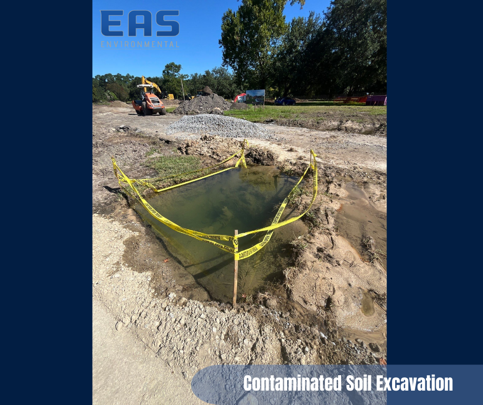 Excavation site with a pool of water inside a yellow-taped area. Soil around, heavy equipment visible.
