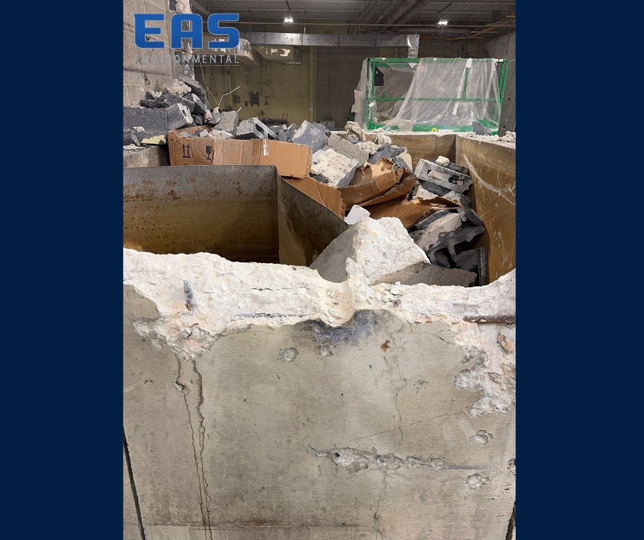 Workers in safety gear on a roof removing material with abatement equipment; urban setting with buildings in background.