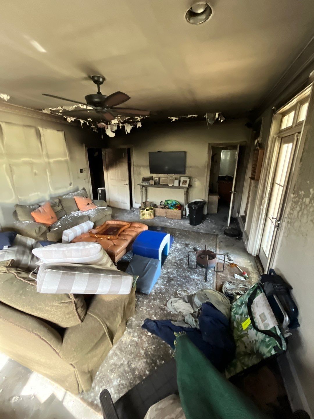 Interior of a smoke-damaged living room; burnt ceiling, debris on the floor, destroyed furniture.