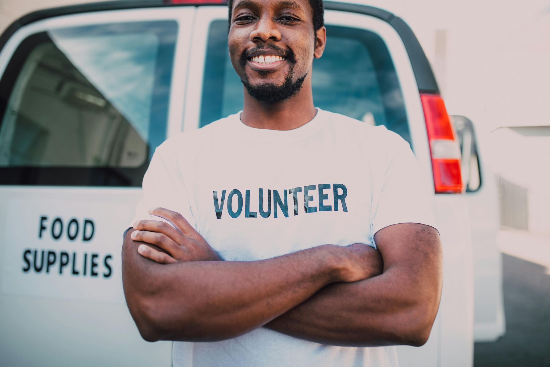 A man wearing a volunteer shirt is standing in front of a food supplies van.