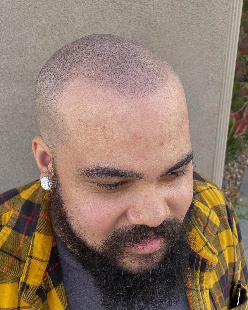 a man with a beard and a bald head is wearing a plaid shirt .