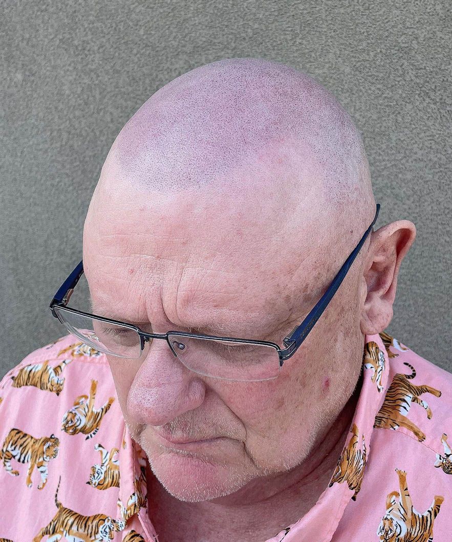 a bald man wearing glasses and a pink shirt with cats on it