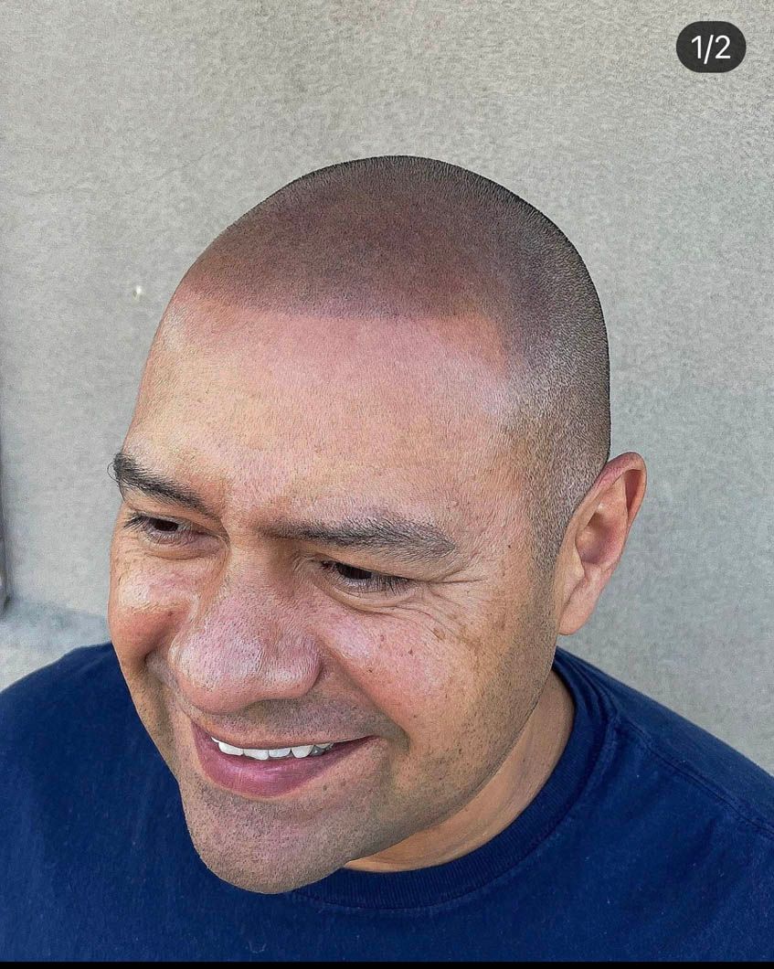 a man with a shaved head is smiling and wearing a blue shirt .