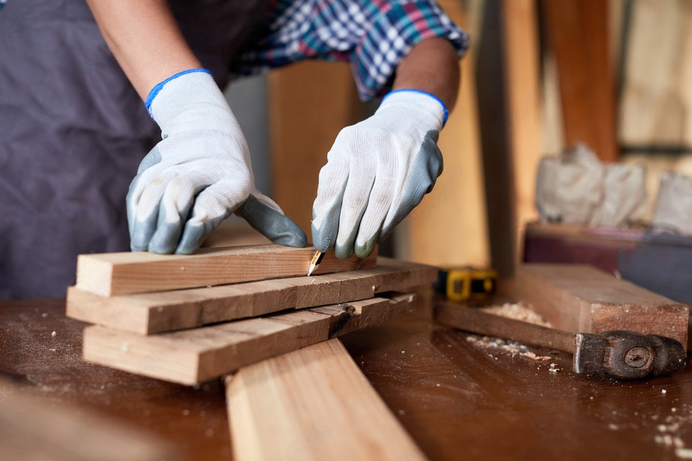 a man wearing gloves is cutting a piece of wood on a table .