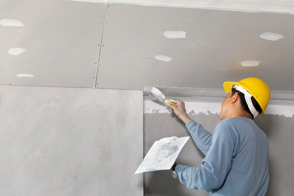 a man wearing a hard hat is plastering a wall .